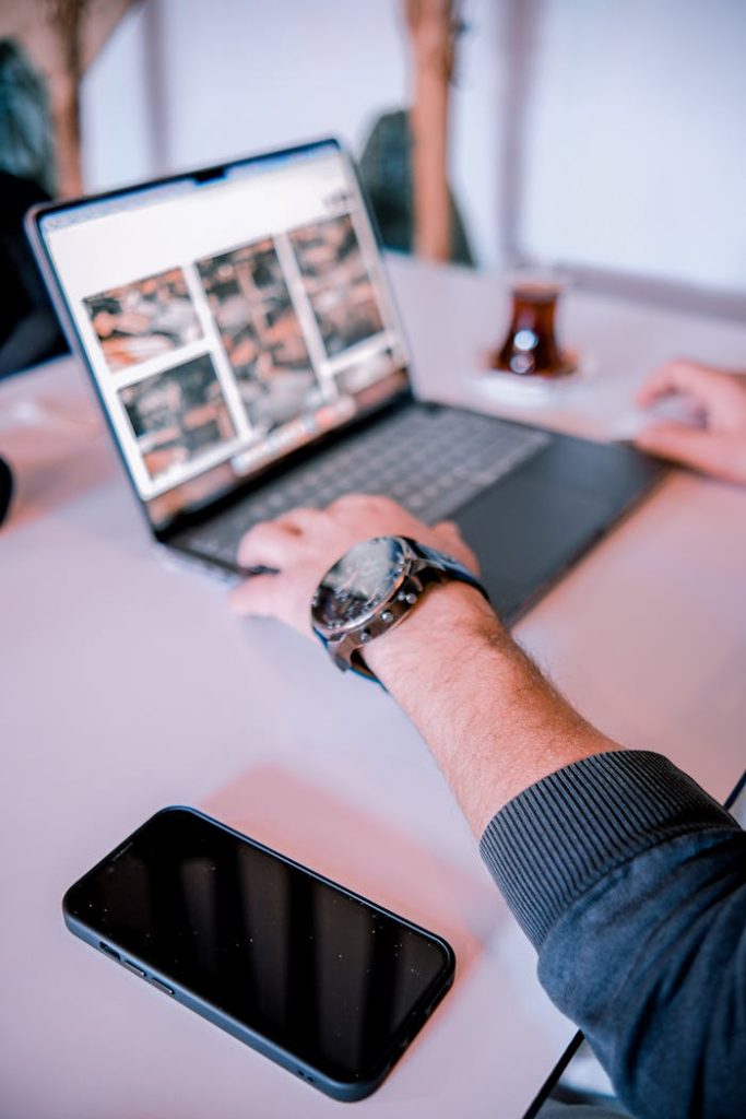Person working on laptop at a desk with smartphone and tea glass nearby.